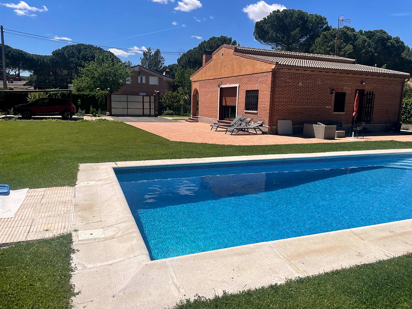 La casa y la piscina entre pinos, con el aparcamiento al fondo